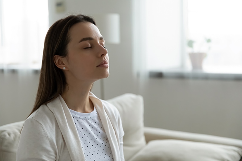 Why Do I Need a Humidifier? Woman sitting on couch with eyes closed.