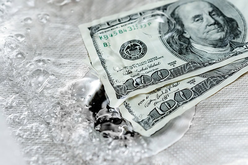 Money flowing down a sink drain.
