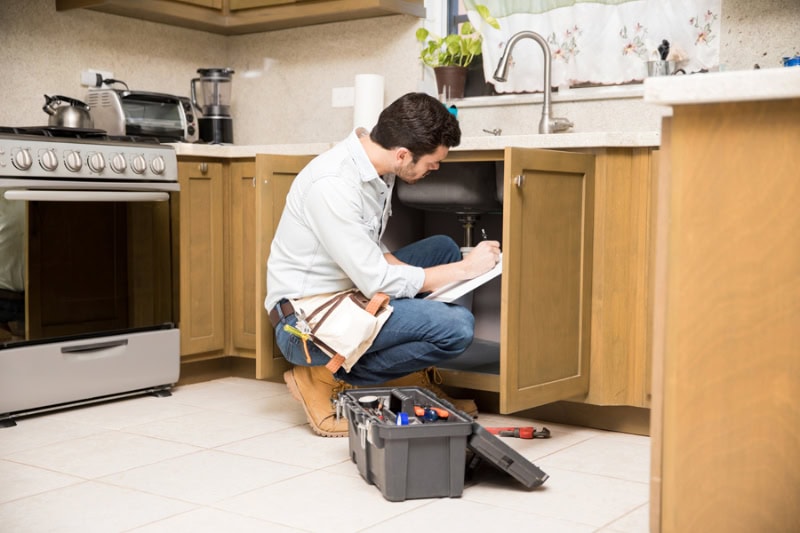 Good looking young handyman looking at a broken sink and writing a work estimate