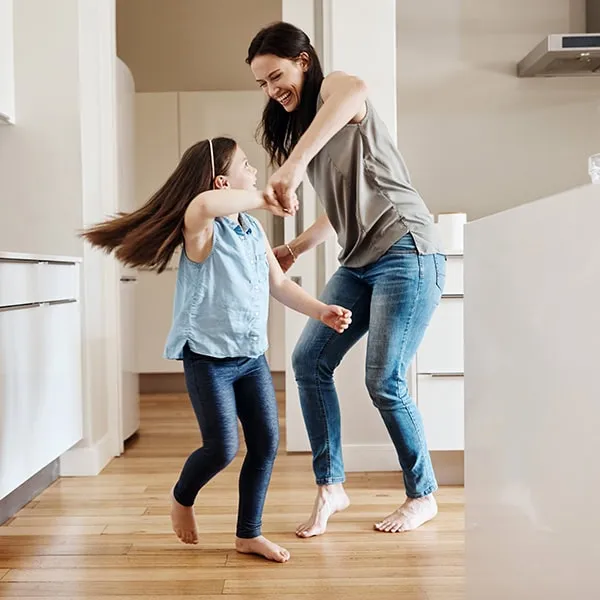 mom and young daughter dancing in their home.